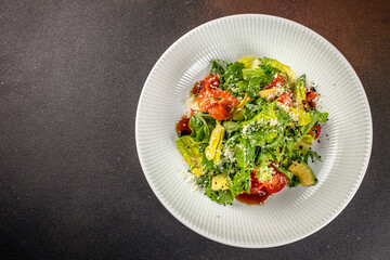 Fresh green salad with arugula, lettuce, avocado, cherry tomatoes, and grated cheese, served with...
