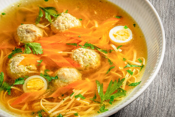 Bowl of clear chicken broth with noodles, meatballs, carrot slices, parsley, and halved quail eggs served as a comforting homemade soup