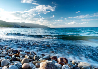 A tranquil pebble beach with rolling waves under a dramatic sky, with lush green hills on the distant coastline.