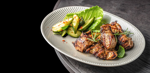 Grilled meat served with fresh cucumber salad, lettuce, and herbs on a striped plate