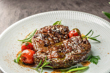 Grilled beef steak garnished with coarse salt, fresh herbs, and roasted cherry tomatoes on a white plate