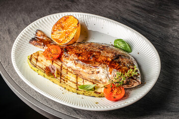 Grilled whole fish served with charred zucchini, roasted tomatoes, and a caramelized lemon on a...