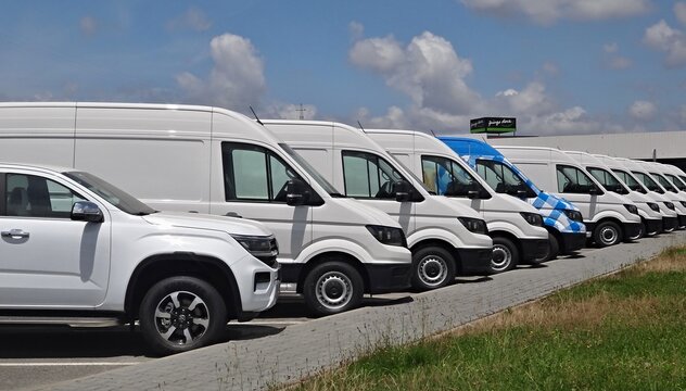 Row of white vans and pickup truck parked in dealership parking lot