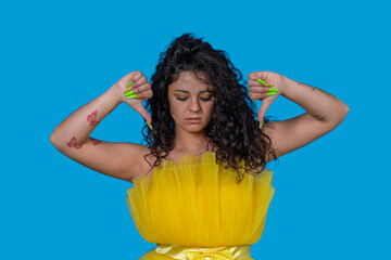 Young woman showing thumbs down gesture expressing dislike on blue background
