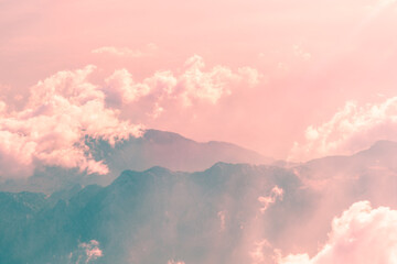 Soft pink clouds gently enveloping rugged mountain peaks create a breathtaking sunset panorama,...