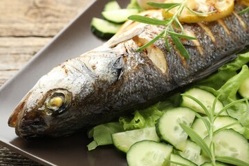 Tasty roasted seabass fish served with vegetables and lemon on wooden table, closeup. Homemade seafood dish