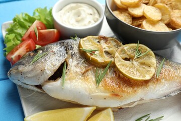 Tasty roasted dorado fish served with vegetables and sauce on light blue wooden table, closeup. Homemade seafood dish