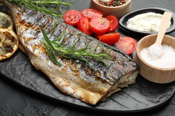 Tasty roasted mackerel served with spices and sauce on black table, closeup. Homemade seafood dish