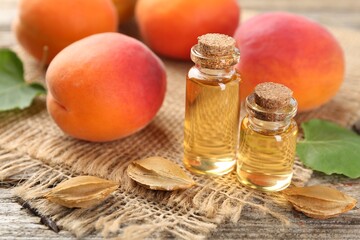 Aromatic essential oil in bottles, seeds and ripe apricots on wooden table, closeup