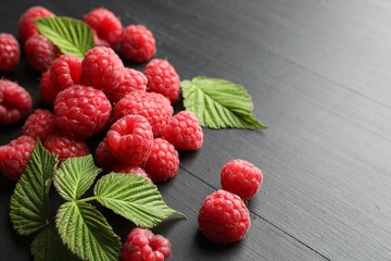 Tasty fresh ripe raspberries and leaves on black table, closeup. Space for text