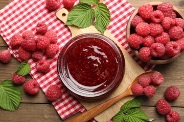 Tasty jam, fresh ripe raspberries and leaves on wooden table, flat lay