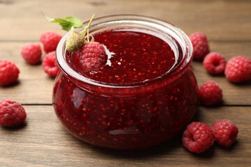 Tasty raspberry jam in glass jar on wooden table, closeup
