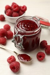 Tasty jam and fresh ripe raspberries on white wooden table, closeup