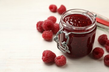 Tasty jam and fresh ripe raspberries on white wooden table, closeup. Space for text