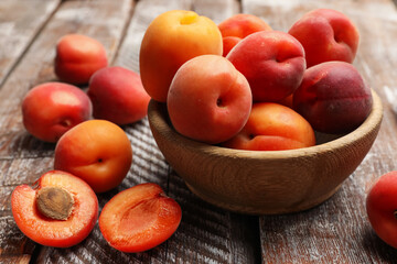 Fresh ripe apricots in bowl on wooden table, closeup