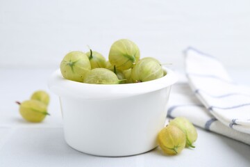 Fresh green gooseberries in bowl on white table, closeup