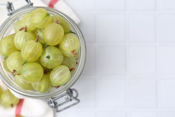 Fresh green gooseberries in jar on white tiled table, top view. Space for text