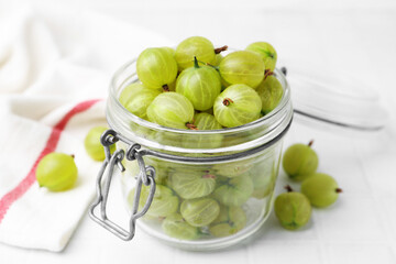 Fresh green gooseberries in jar on white table, closeup