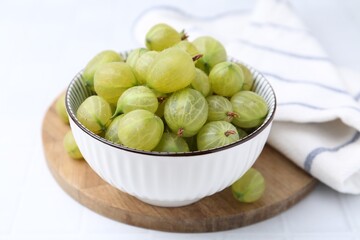 Fresh green gooseberries in bowl on white table, closeup