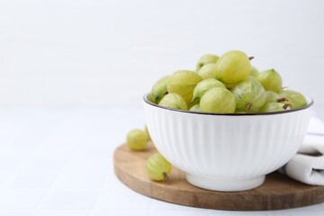 Fresh green gooseberries in bowl on white table, closeup. Space for text