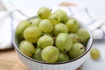 Fresh green gooseberries in bowl on white table, closeup