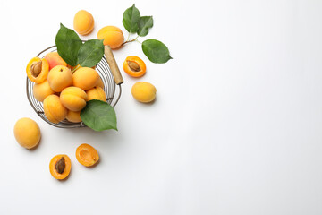 Fresh apricots, green leaves and metal basket on white background, flat lay. Space for text