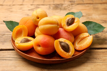 Many fresh apricots and green leaves on wooden table, closeup
