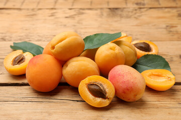Pile of fresh apricots and green leaves on wooden table, closeup