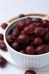 Ripe red gooseberries in bowl on white table, closeup
