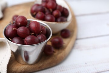 Ripe red gooseberries in bowl on white wooden table, closeup. Space for text