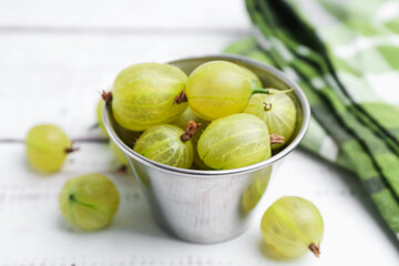 Ripe green gooseberries in bowl on white wooden table, closeup