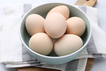 Raw chicken eggs in bowl on white table, closeup