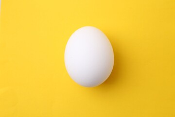 One raw chicken egg on yellow background, top view
