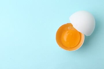 One broken chicken egg on light blue background, top view. Space for text