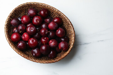 Ripe cherry plums in wicker basket on white marble table, top view. Space for text