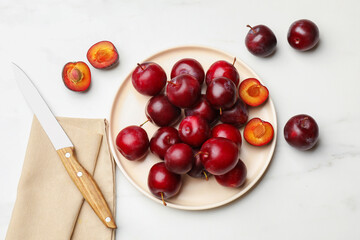 Ripe cherry plums and knife on white marble table, flat lay