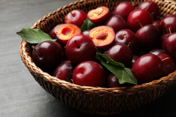 Ripe cherry plums and green leaves in wicker basket on dark textured table, closeup