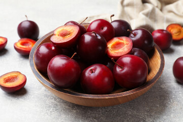 Whole, cut cherry plums in bowl on grey textured table, closeup