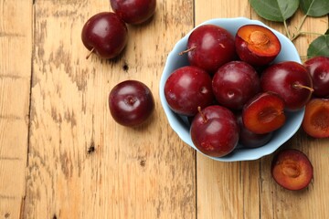 Ripe cherry plums and bowl on wooden table, flat lay. Space for text