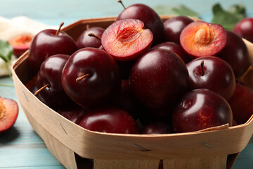 Whole and cut cherry plums in basket on light blue wooden table, closeup