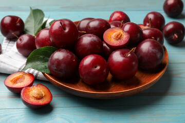 Whole and cut cherry plums on light blue wooden table, closeup