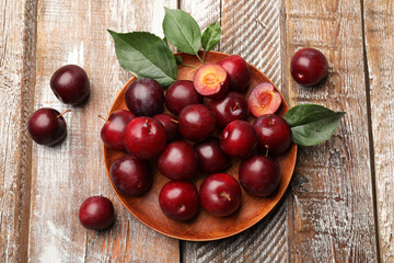 Whole, cut cherry plums and green leaves on color wooden table, flat lay