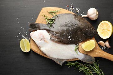 Fresh raw flounder fish and spices on black wooden table, flat lay. Seafood