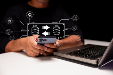 A person interfaces with a smartphone and laptop, surrounded by data transfer graphics,...
