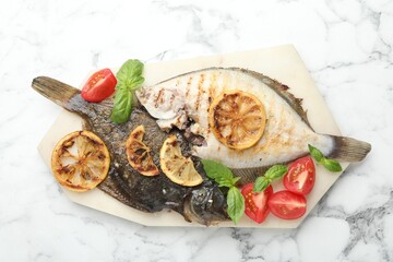 Tasty roasted flounder fish served with tomatoes, basil and lemon slices on white marble table, top view. Homemade seafood dish