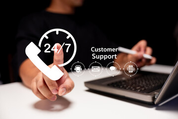 A person gestures towards a 24/7 customer support graphic while using a laptop, symbolizing...