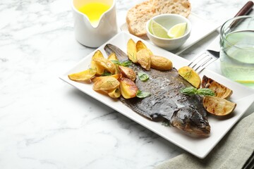 Homemade seafood dish. Tasty roasted flounder fish served with potatoes, basil and lemon slices on white marble table, closeup. Space for text