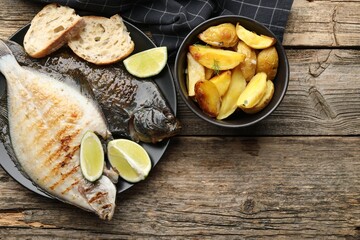 Homemade seafood dish. Tasty roasted flounder fish served with potatoes, bread and lime slices on wooden table, flat lay. Space for text