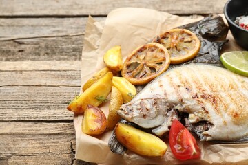 Tasty roasted flounder fish served with potatoes, tomatoes and lemon slices on wooden table, closeup. Homemade seafood dish