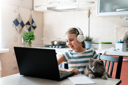 Happy school girl in headphones and cat using laptop at home. Distance learning, online education, homeschooling. Kids and gadgets, technology. Therapy, speech session for child and pet, video chat